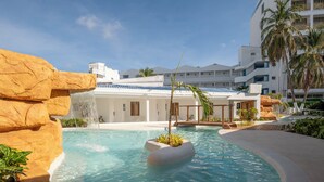 A pool with a waterfall feature, surrounded by palm trees and a building with balconies. - Hotel El Dorado (San Andrés)