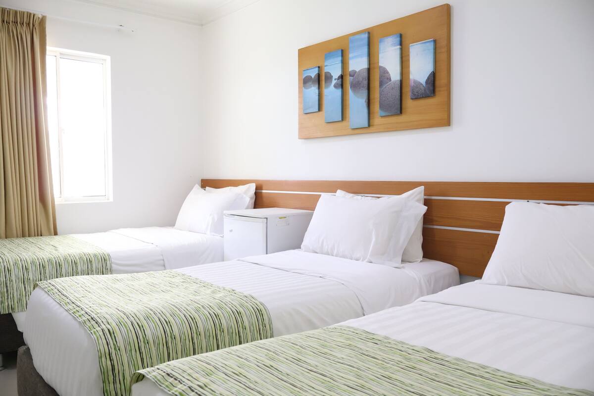 A hotel room with two beds, a wooden headboard, a nightstand, and a window with curtains.