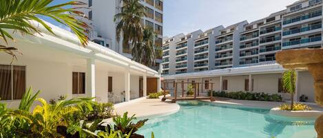 A hotel courtyard with a swimming pool, palm trees, and modern buildings.