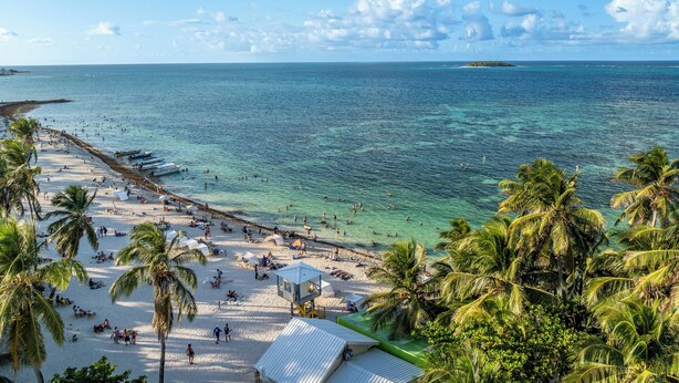 A beach with clear turquoise water, palm trees, and a lifeguard tower. - Hotel El Dorado (San Andrés)