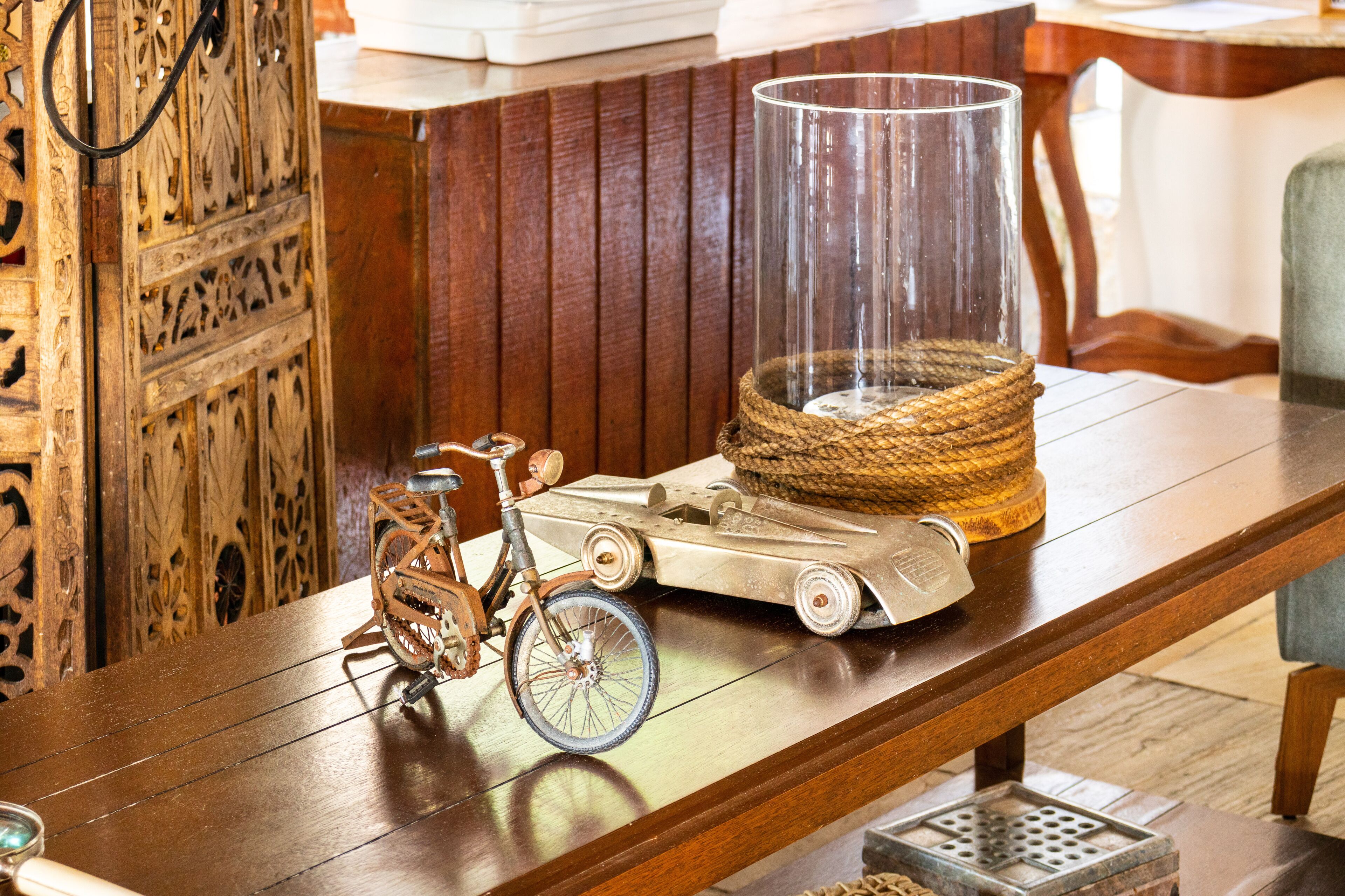 Una mesa de madera con una bicicleta antigua, un coche modelo y un florero transparente con una cesta tejida.