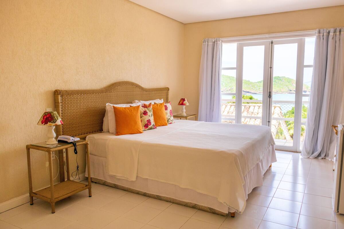 A bedroom with a large bed, a wicker nightstand, a lamp, and a view of a balcony.