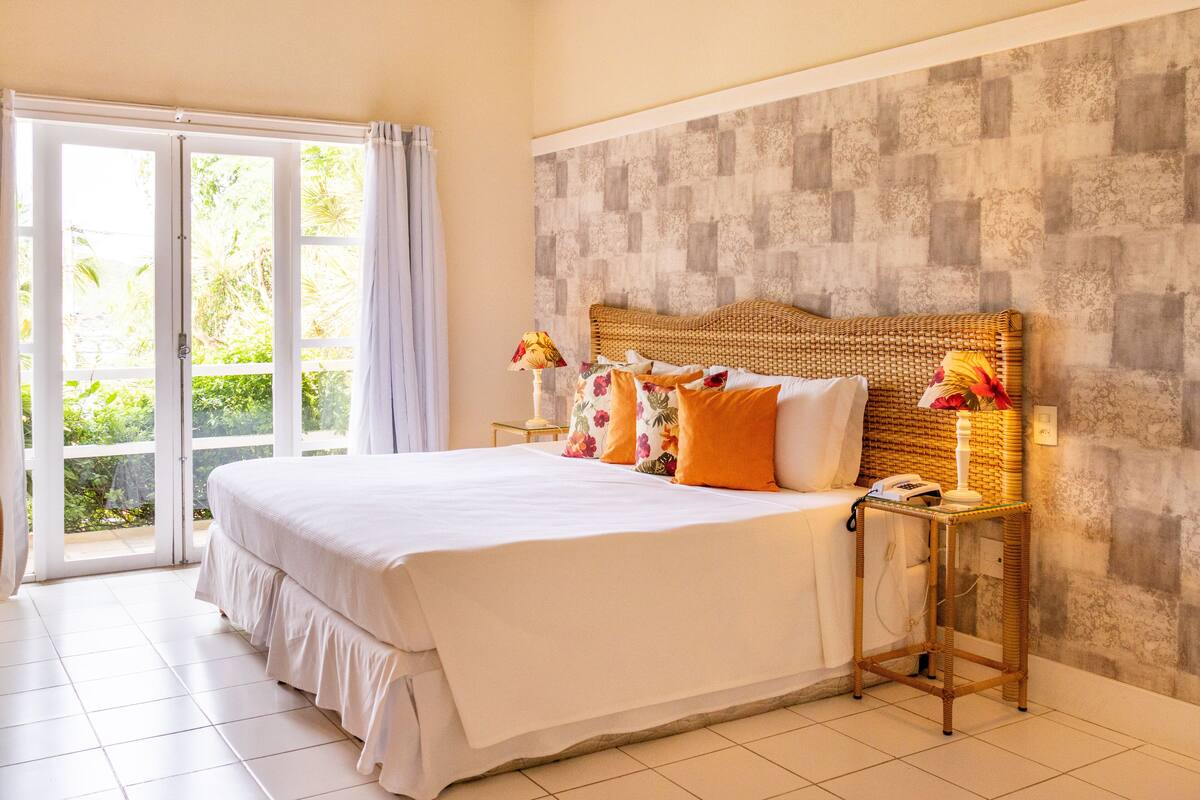 A bedroom with a large bed, a wicker headboard, and a view through a sliding glass door to a balcony.
