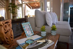 A cozy living area with a striped sofa, a wooden coffee table with a book, a magnifying glass, and two potted plants.