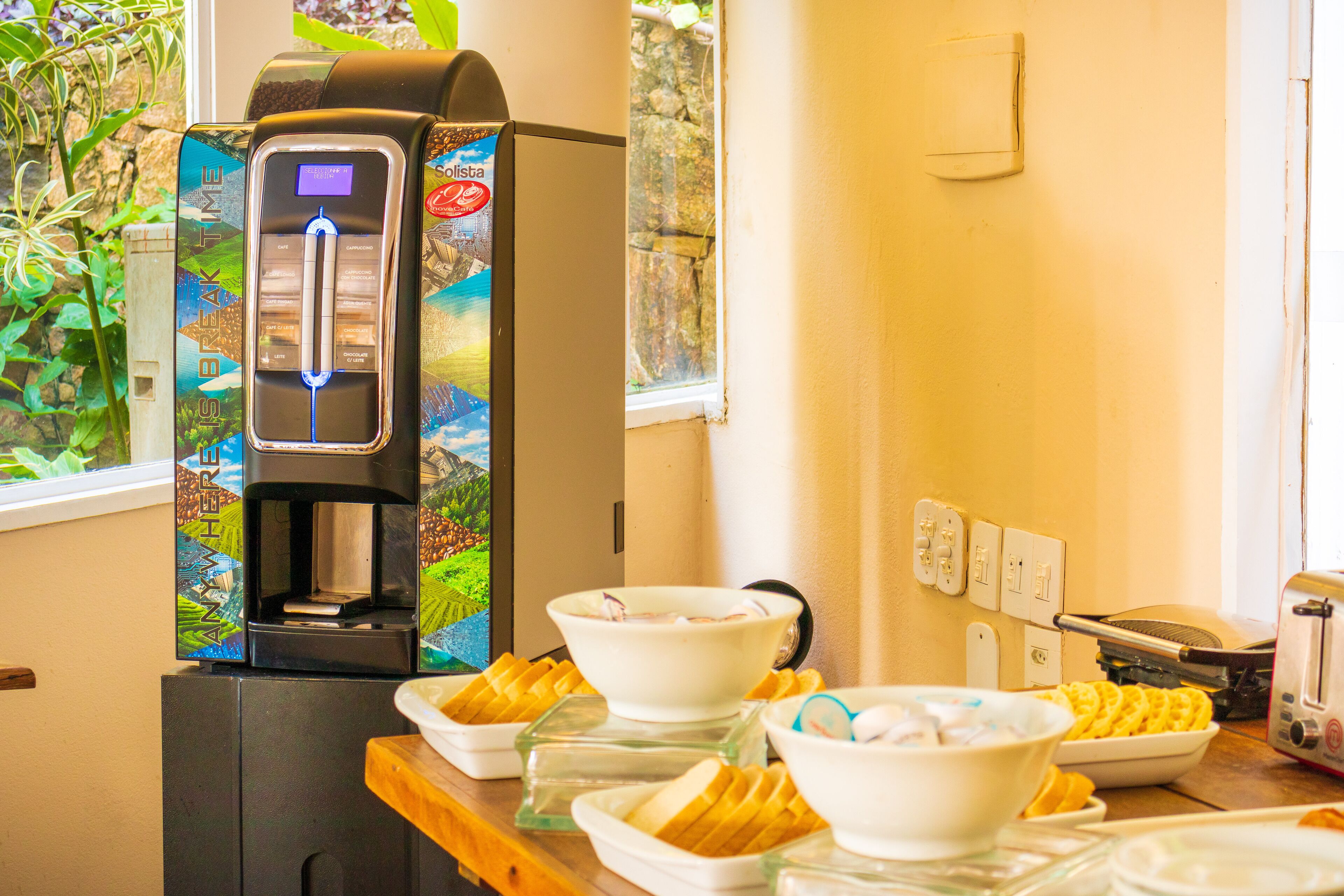 A breakfast setup with a coffee machine, bowls of cereal, and toast.