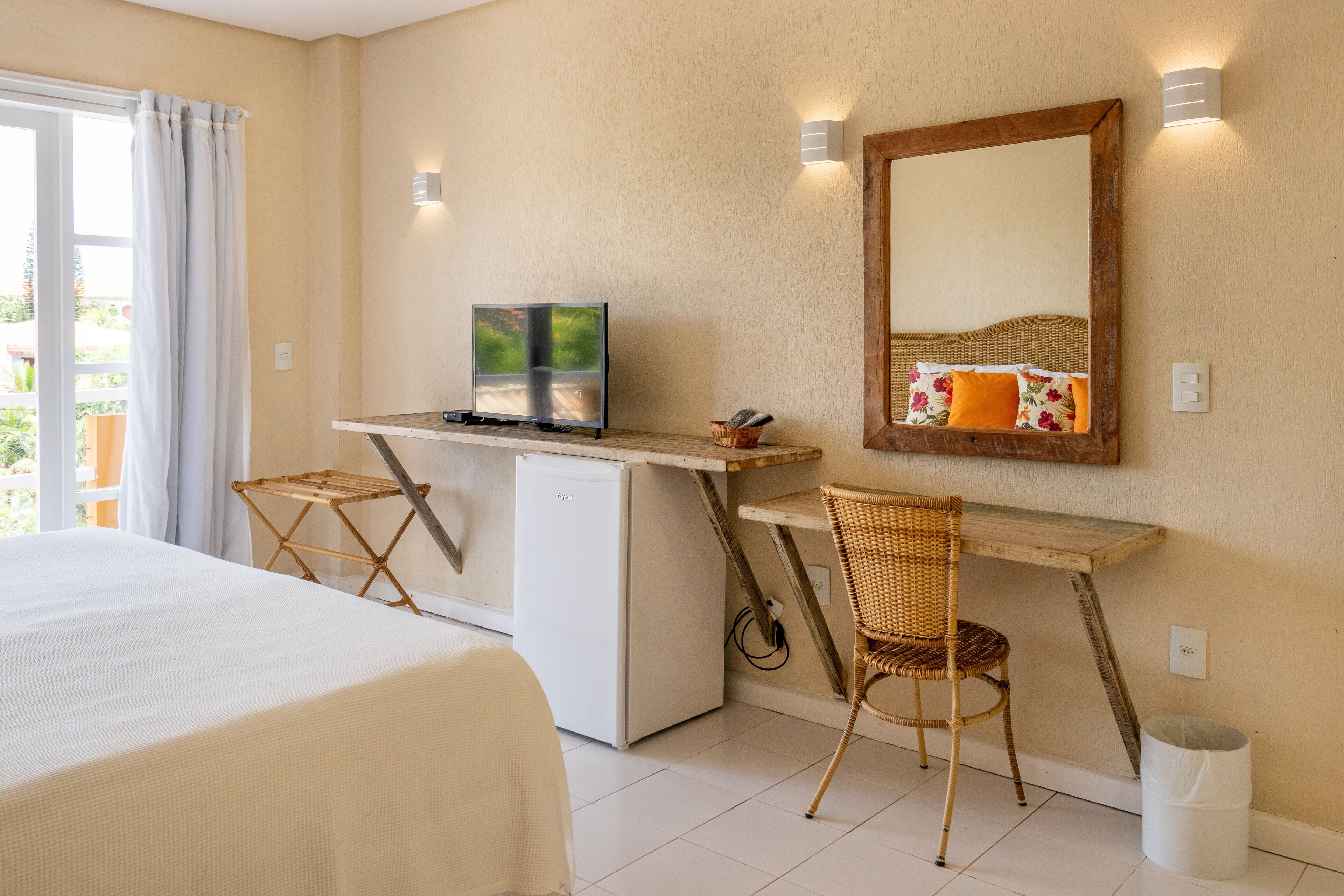 A bedroom with a bed, a desk with a computer, a chair, and a small refrigerator.