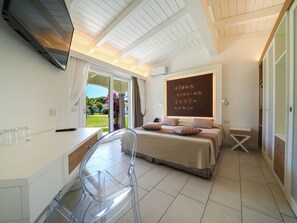 A bedroom with a bed, a desk, a chair, a wardrobe, and a view of the garden.