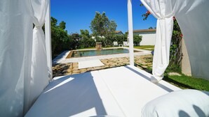 Un espacio al aire libre techado con piscina, cortinas blancas y cielo azul despejado.