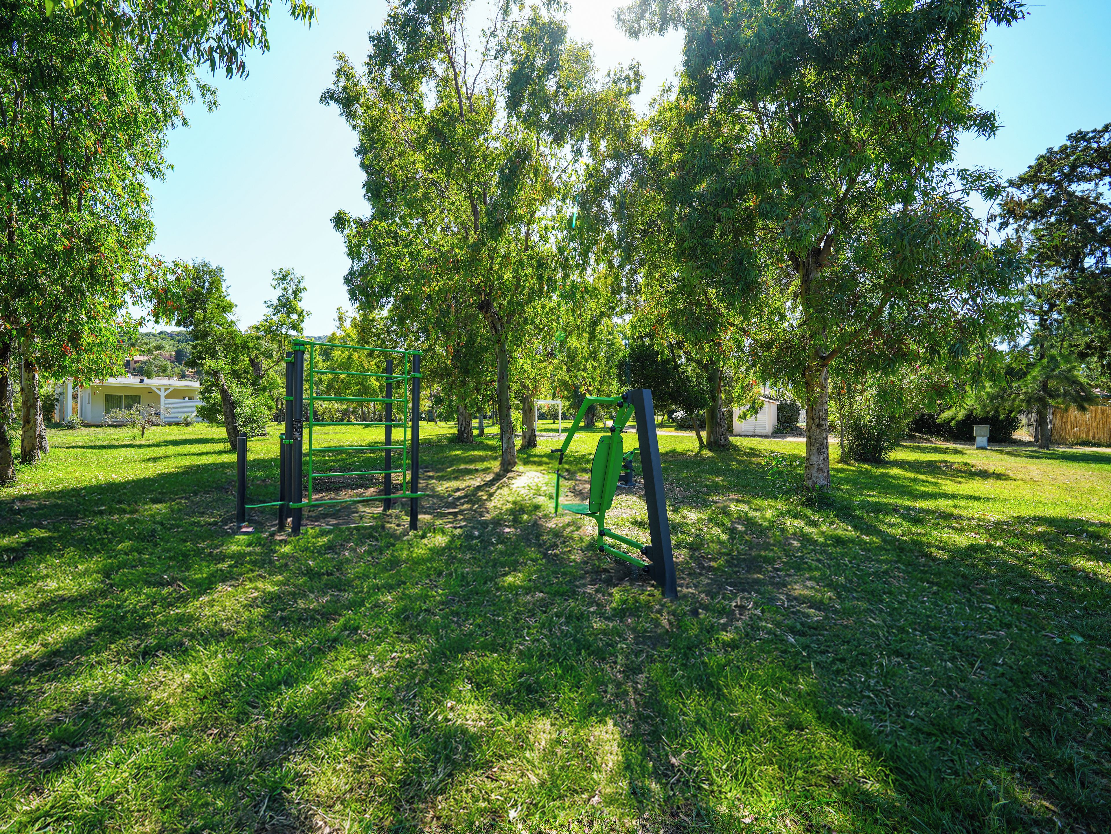 A park with green exercise equipment, trees, and a grassy area.
