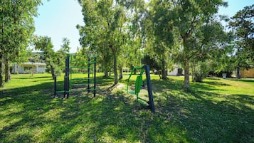 A park with green exercise equipment, trees, and a grassy area.