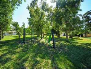 Um parque com equipamentos de ginástica verdes, árvores e uma área gramada.