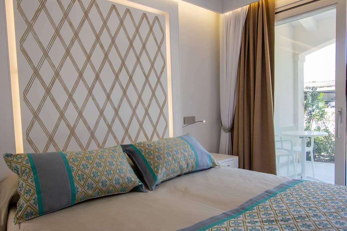Una habitación de hotel con cama, almohadones estampados, diseño geométrico en la pared y vistas al exterior.