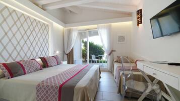 A hotel room with a bed, a desk, a chair, a TV, and a balcony with a view of greenery.