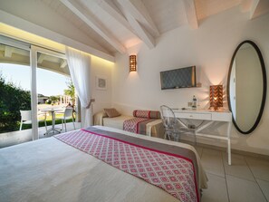 Quarto de hotel com cama, escrivaninha, cadeira, televisão e varanda com vista.