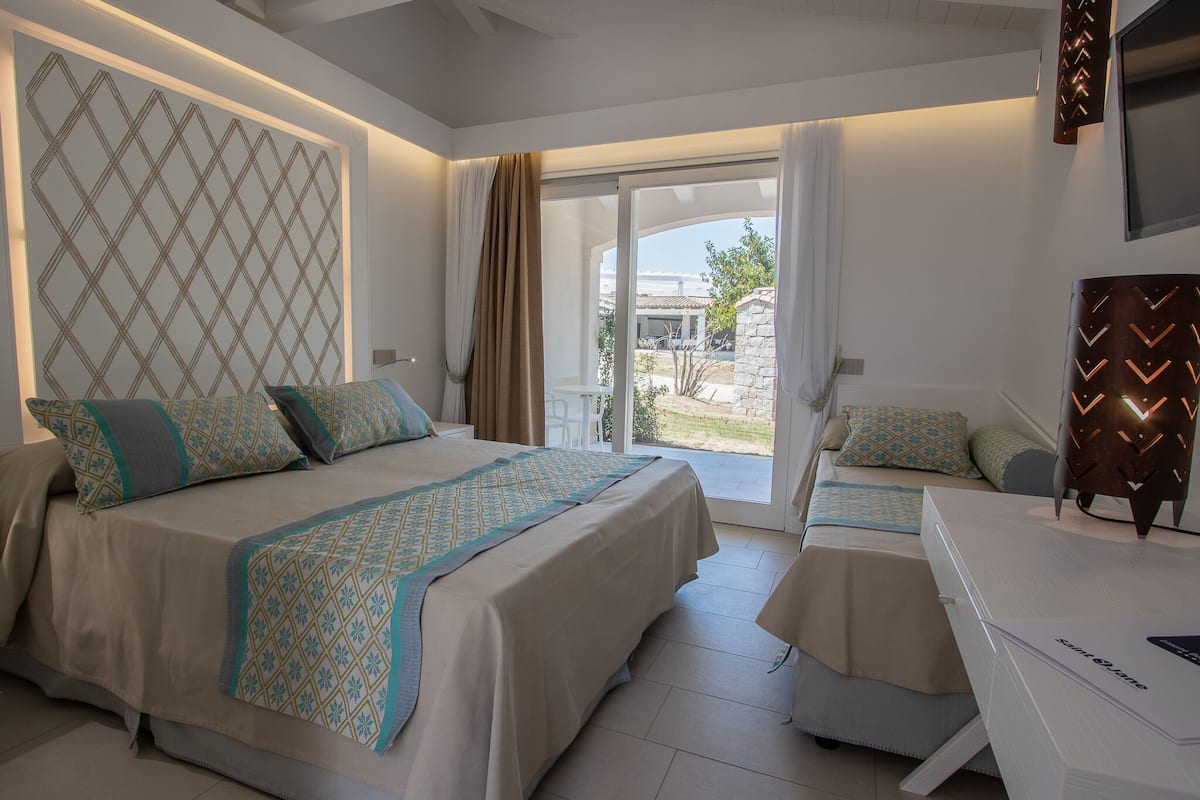 Habitación de hotel con dos camas, un escritorio y un balcón con vistas.