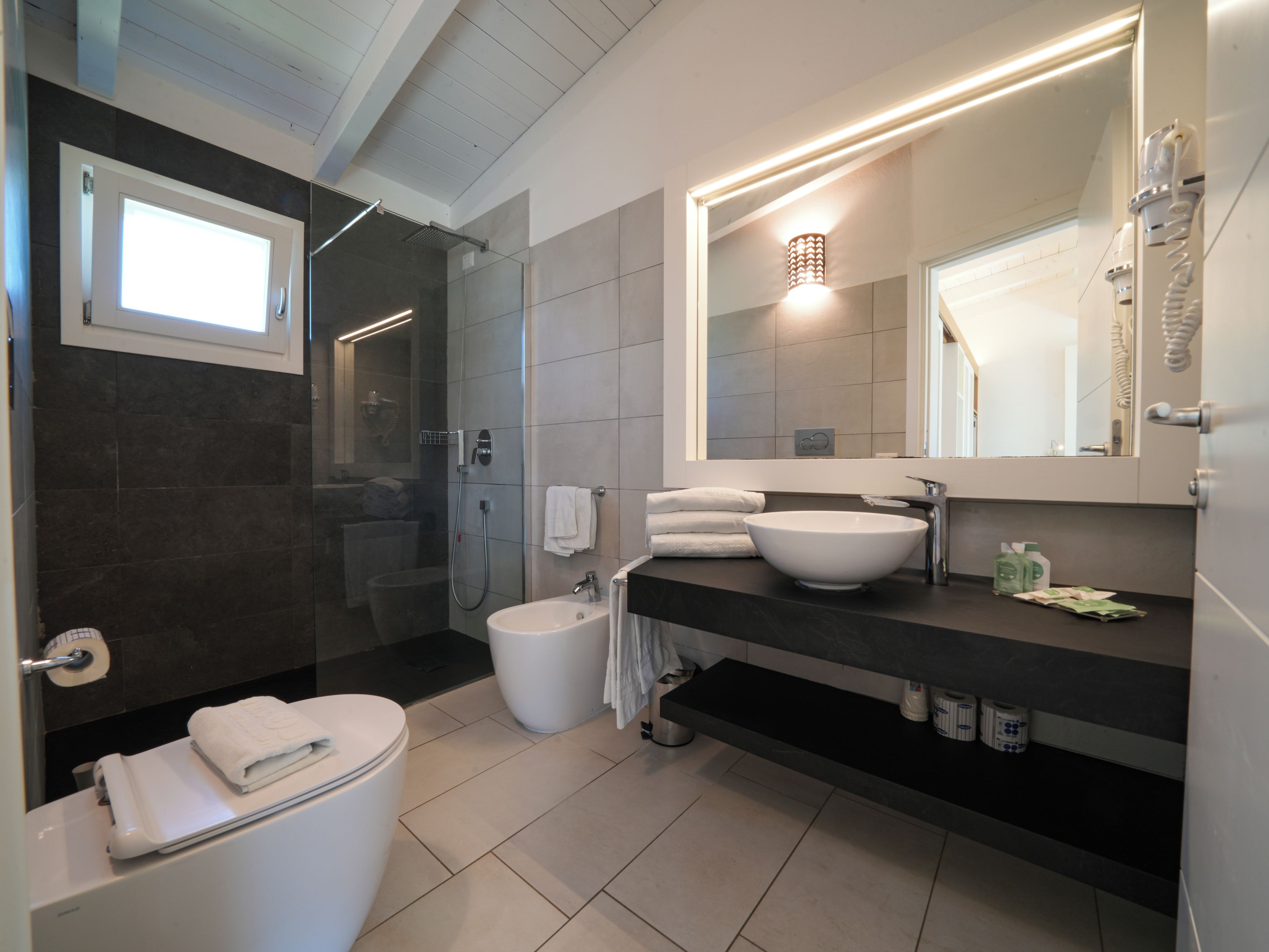 A modern bathroom with a toilet, bidet, sink, and shower.