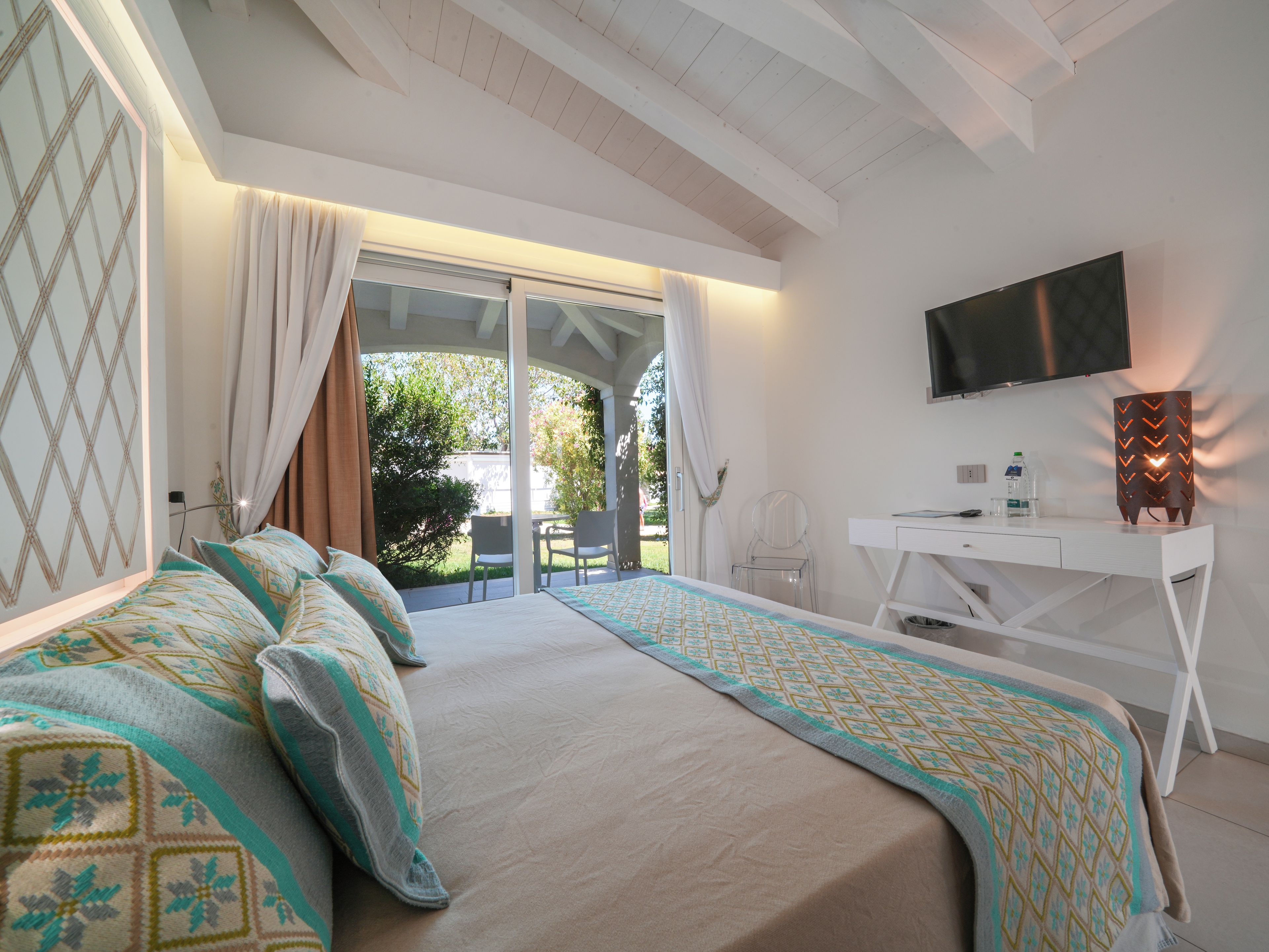 Una camera da letto con un letto, una scrivania, una sedia, una TV e un balcone vista verde.