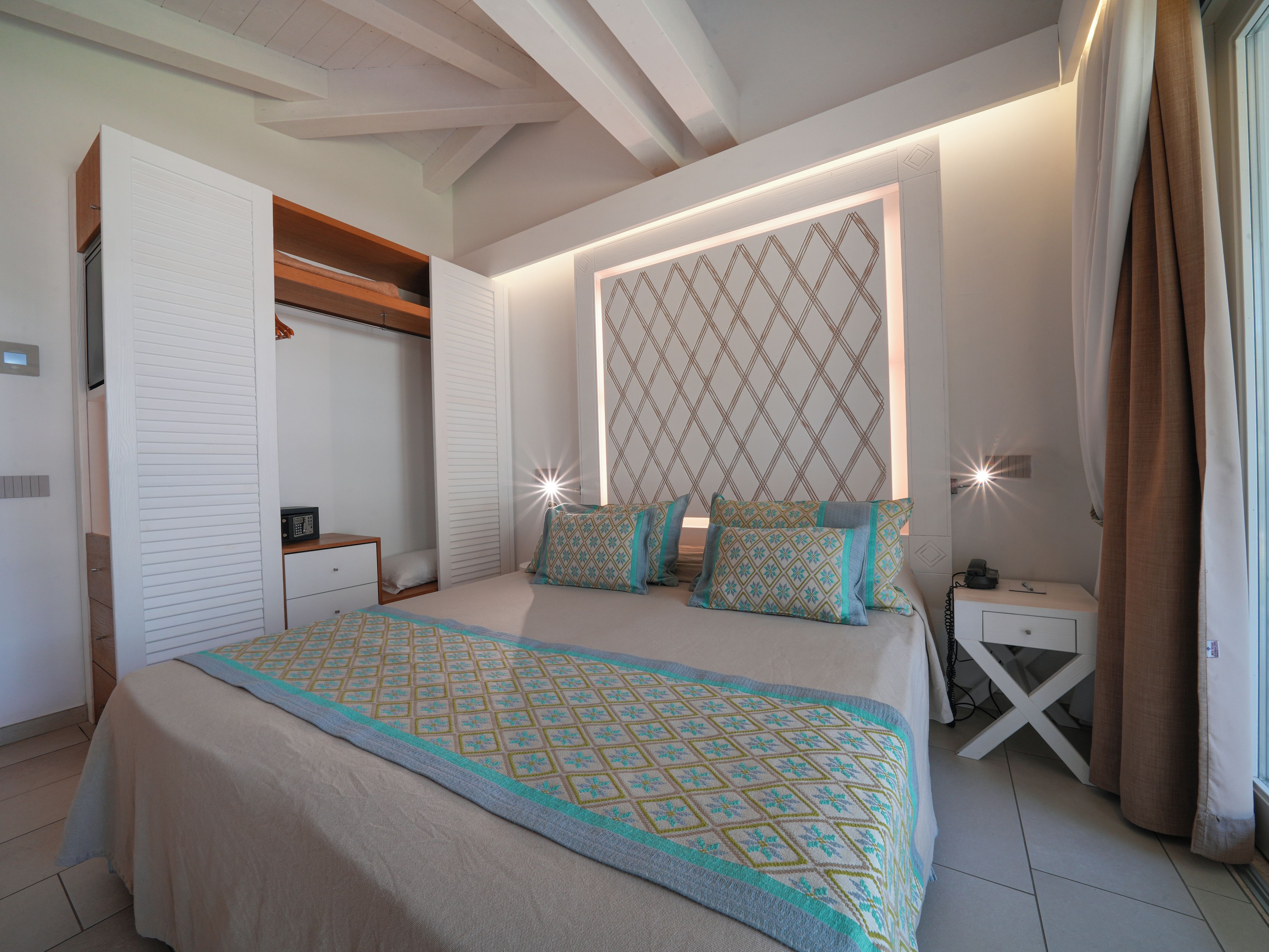 A bedroom with a bed, bedside tables, a wardrobe, and a patterned headboard.