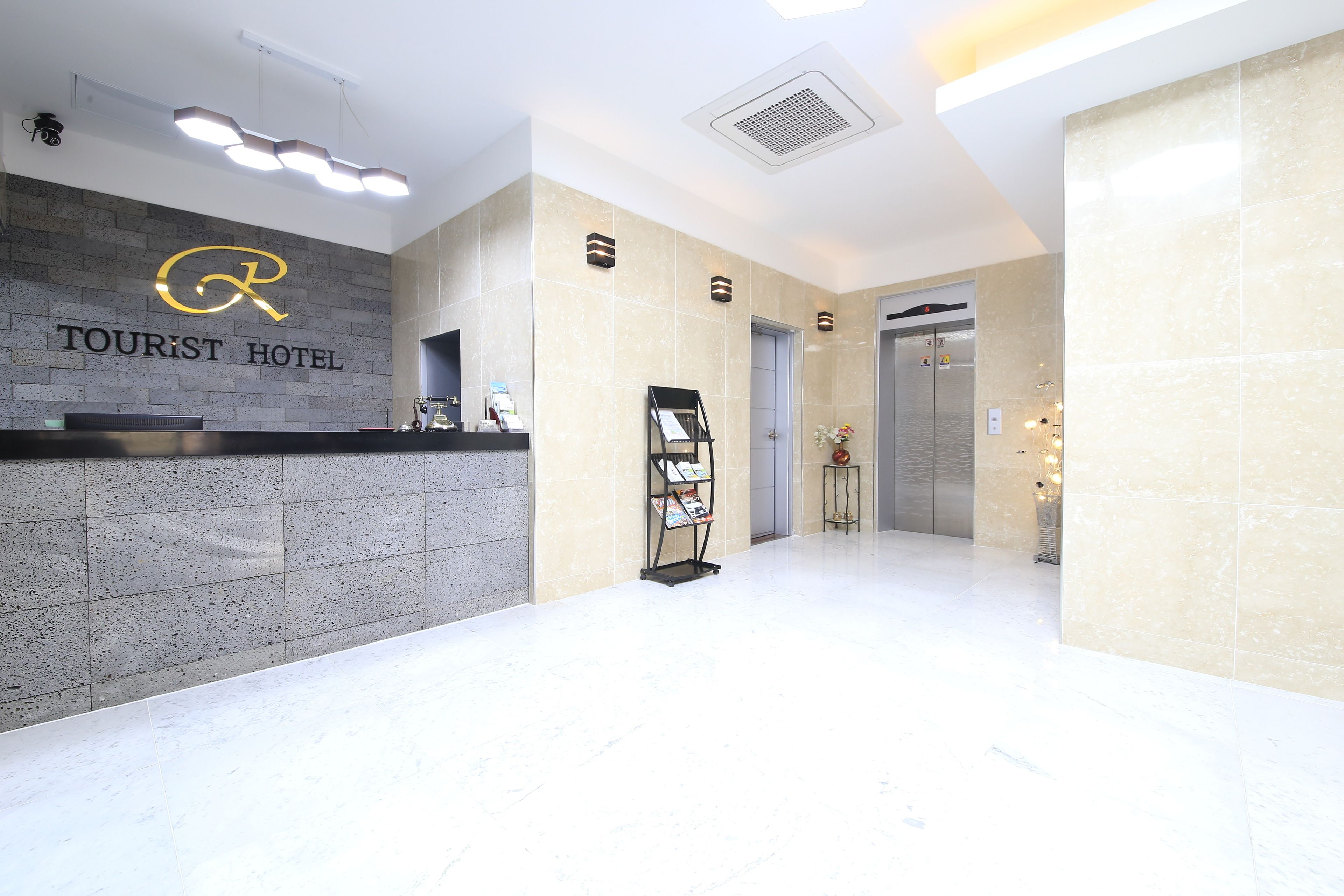 A lobby with a reception desk, a wall-mounted sign reading "TOURIST HOTEL", and a reception area with a small table and a plant.