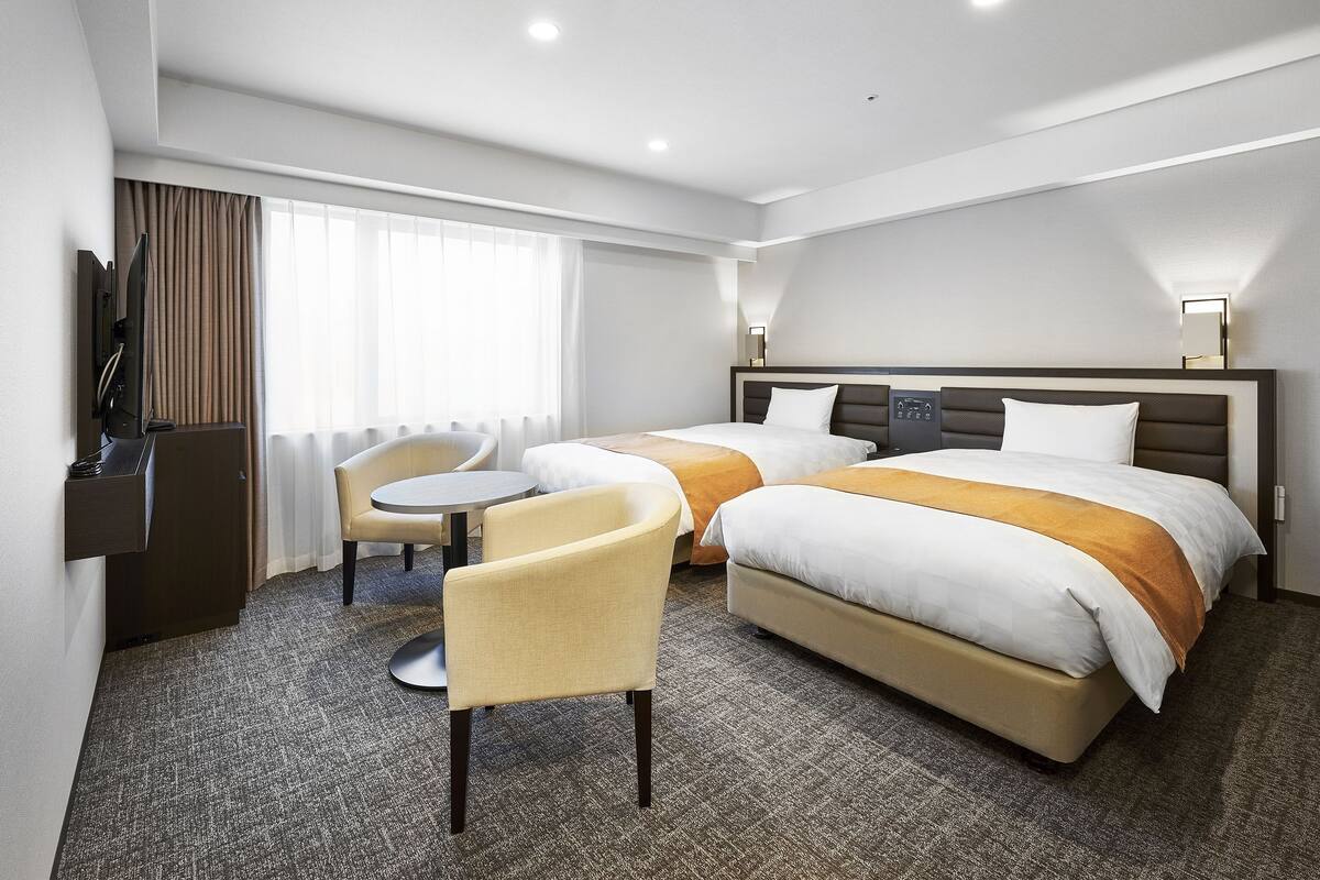 A hotel room with two beds, a desk, a chair, a TV, and a window with curtains.