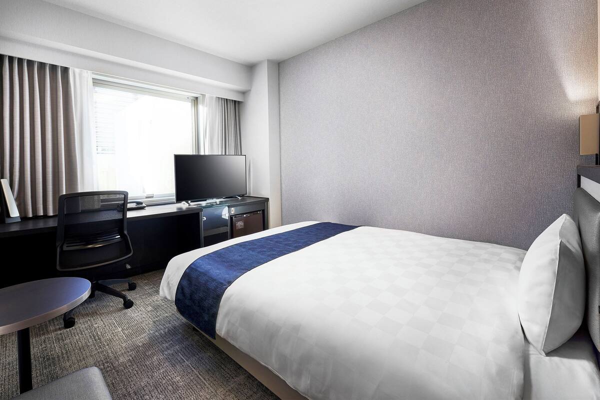 A hotel room with a bed, a desk with a computer, a chair, and a television.