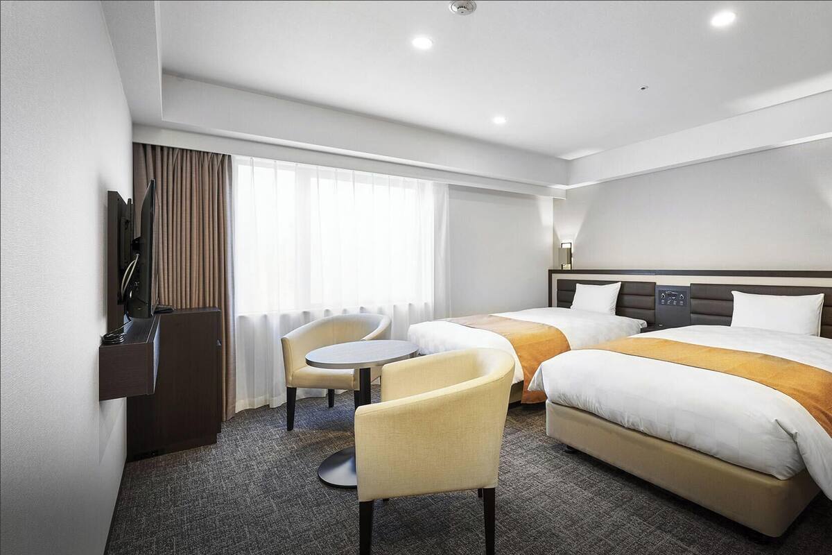A hotel room with two beds, a desk, a chair, and a television.