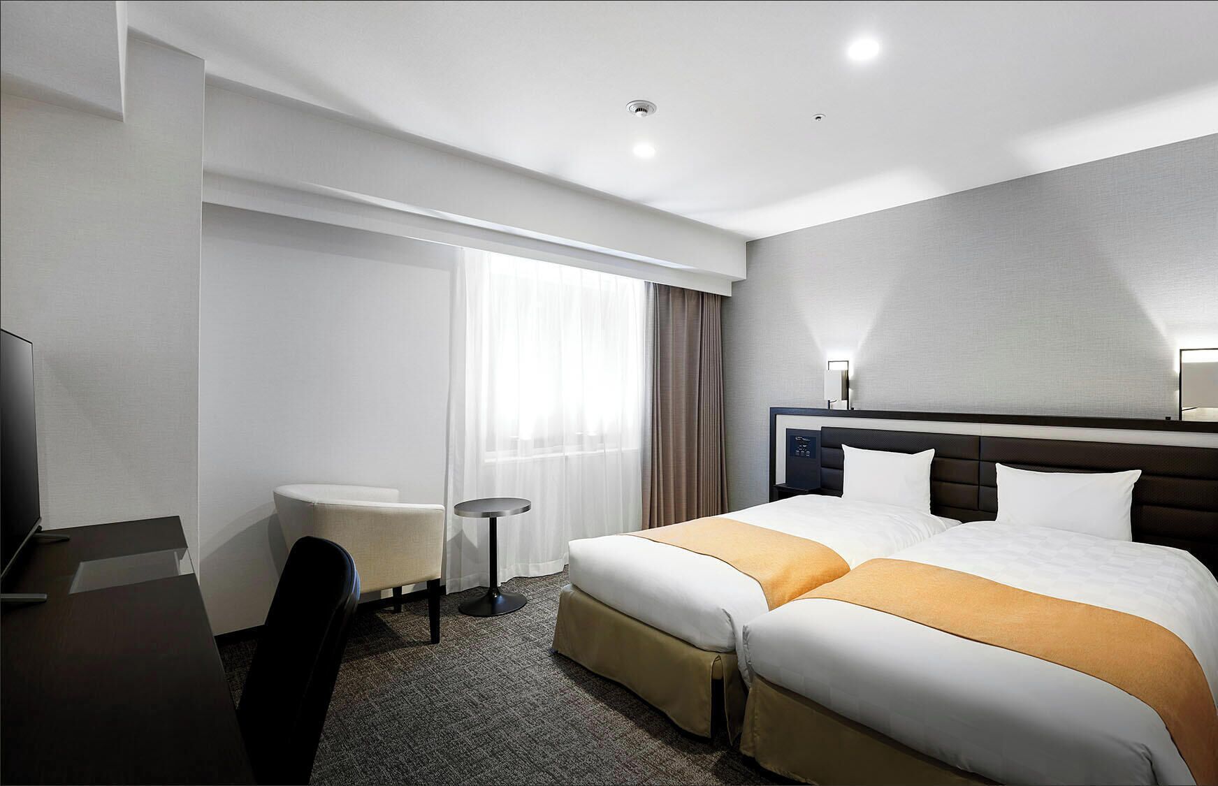 Habitación de hotel con cama, escritorio, silla, mesita y ventana con cortinas.