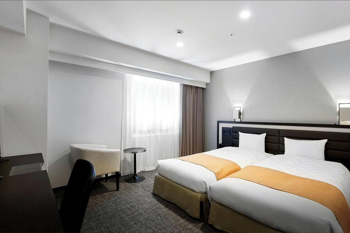 A hotel room with a bed, a desk, a chair, a small table, and a window with curtains.