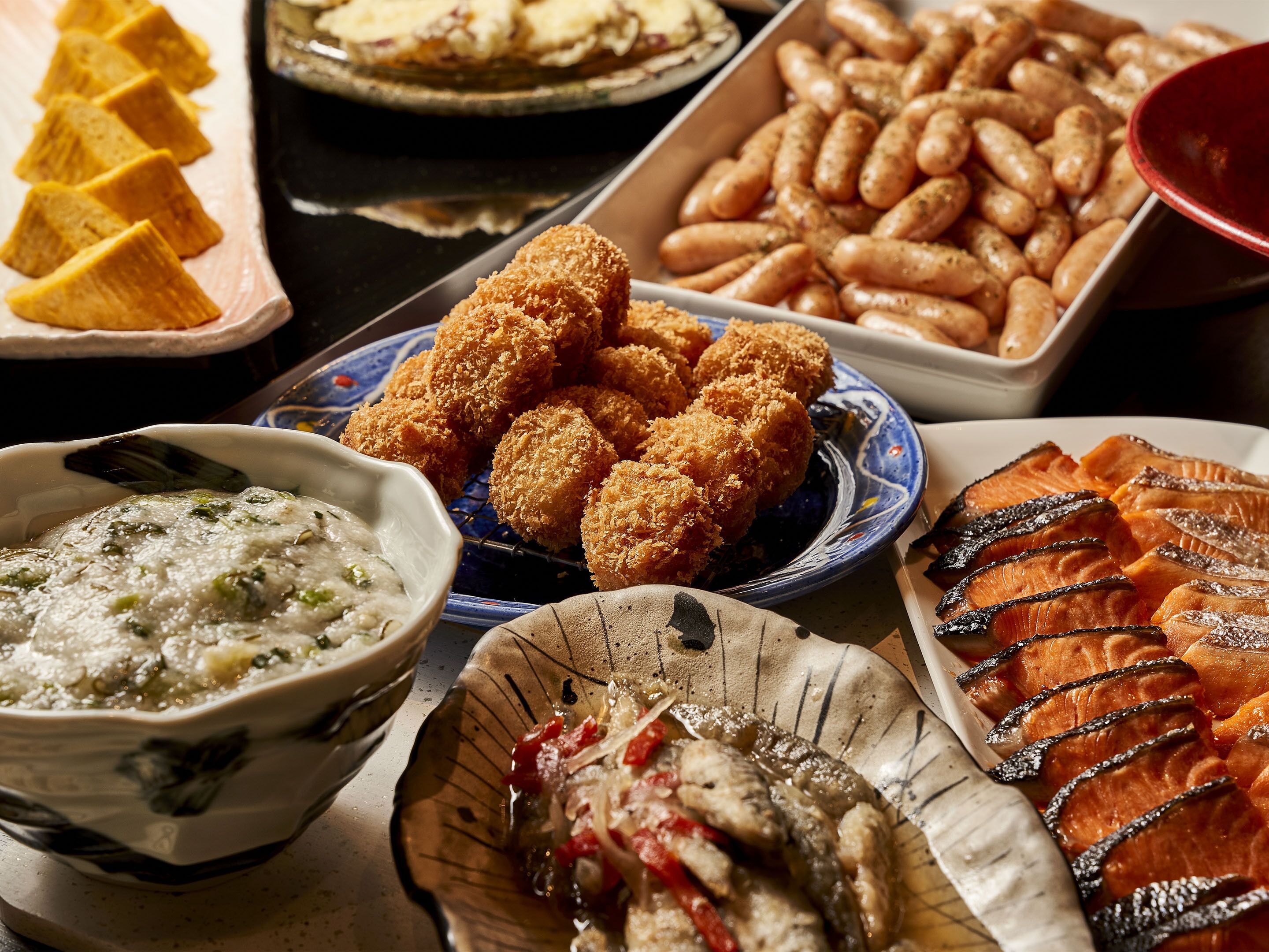 Ein reichhaltiges Buffet mit verschiedenen Speisen, darunter frittierte Gerichte, Lachs und eine Suppe.