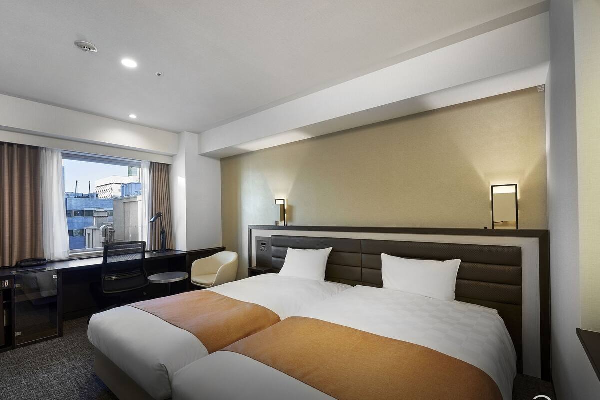 A hotel room with a large bed, a desk, a chair, and a view of the cityscape.