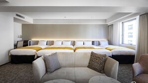 Ein Hotelzimmer mit einem großen Bett, einer Couch, zwei runden Tischen und einem Vorhangfenster.