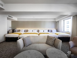 Quarto de hotel com uma cama grande, um sofá, duas mesas redondas e uma janela com cortinas.
