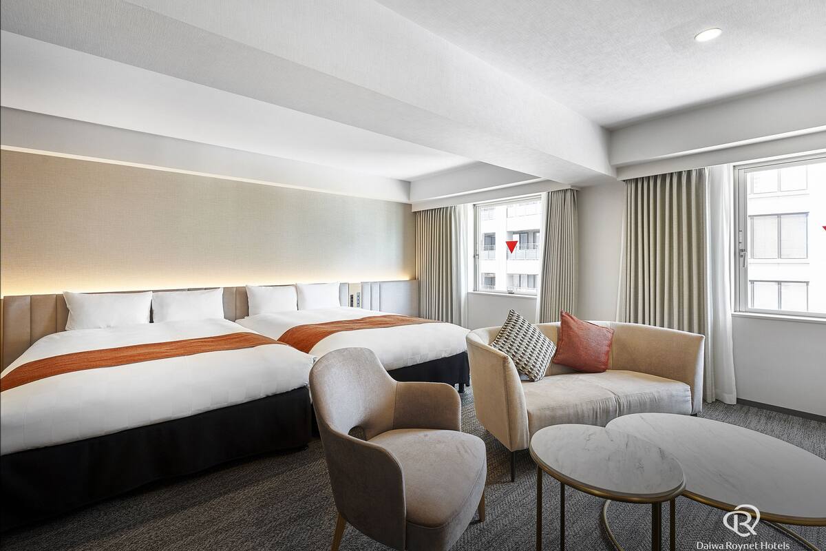 A hotel room with two beds, a sofa, a chair, and a small table.