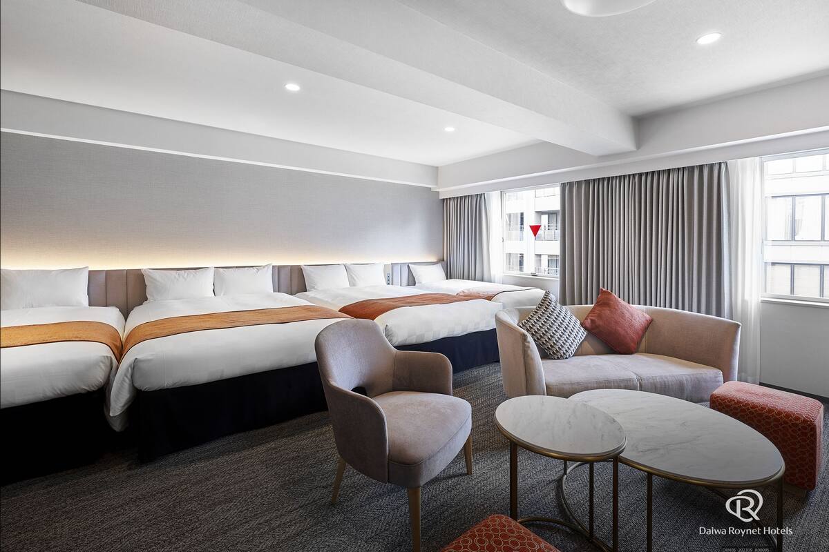A hotel room with two beds, a sofa, a coffee table, and a view of the city.