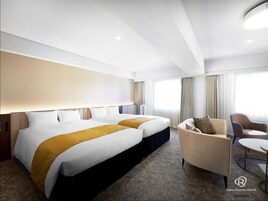 A hotel room with two beds, a sofa, a small table, and a large window with curtains.