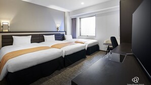 Ein Hotelzimmer mit zwei Betten, einem Schreibtisch, einem Stuhl, einem Fernseher und einem Fenster mit Vorhängen.