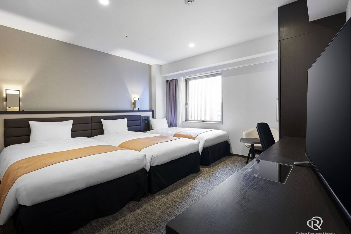 A hotel room with two beds, a desk, a chair, a TV, and a window with curtains.