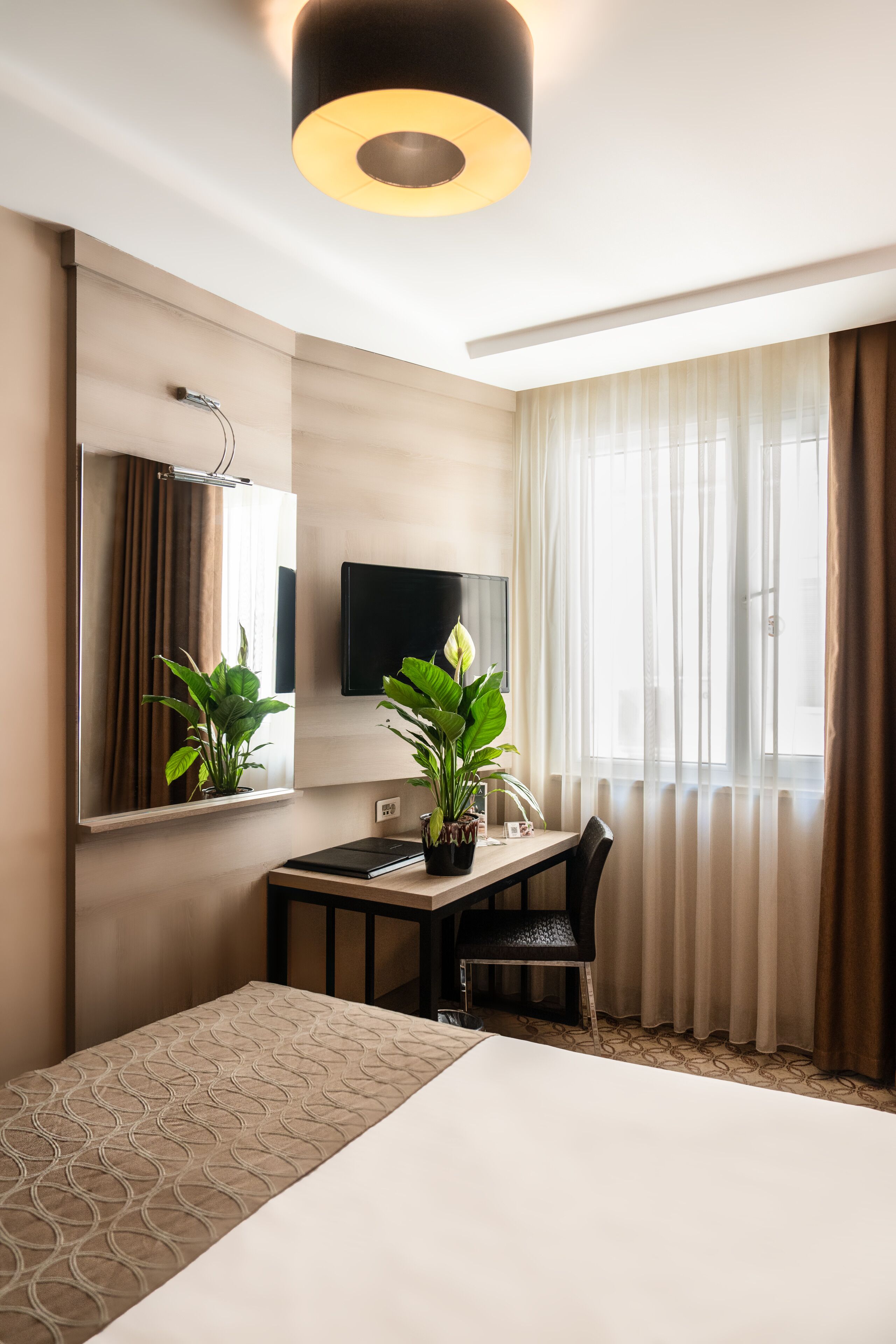 Ein Hotelzimmer mit einem Bett, einem Schreibtisch, einem Sessel, einem Fernseher und zwei Zimmerpflanzen.
