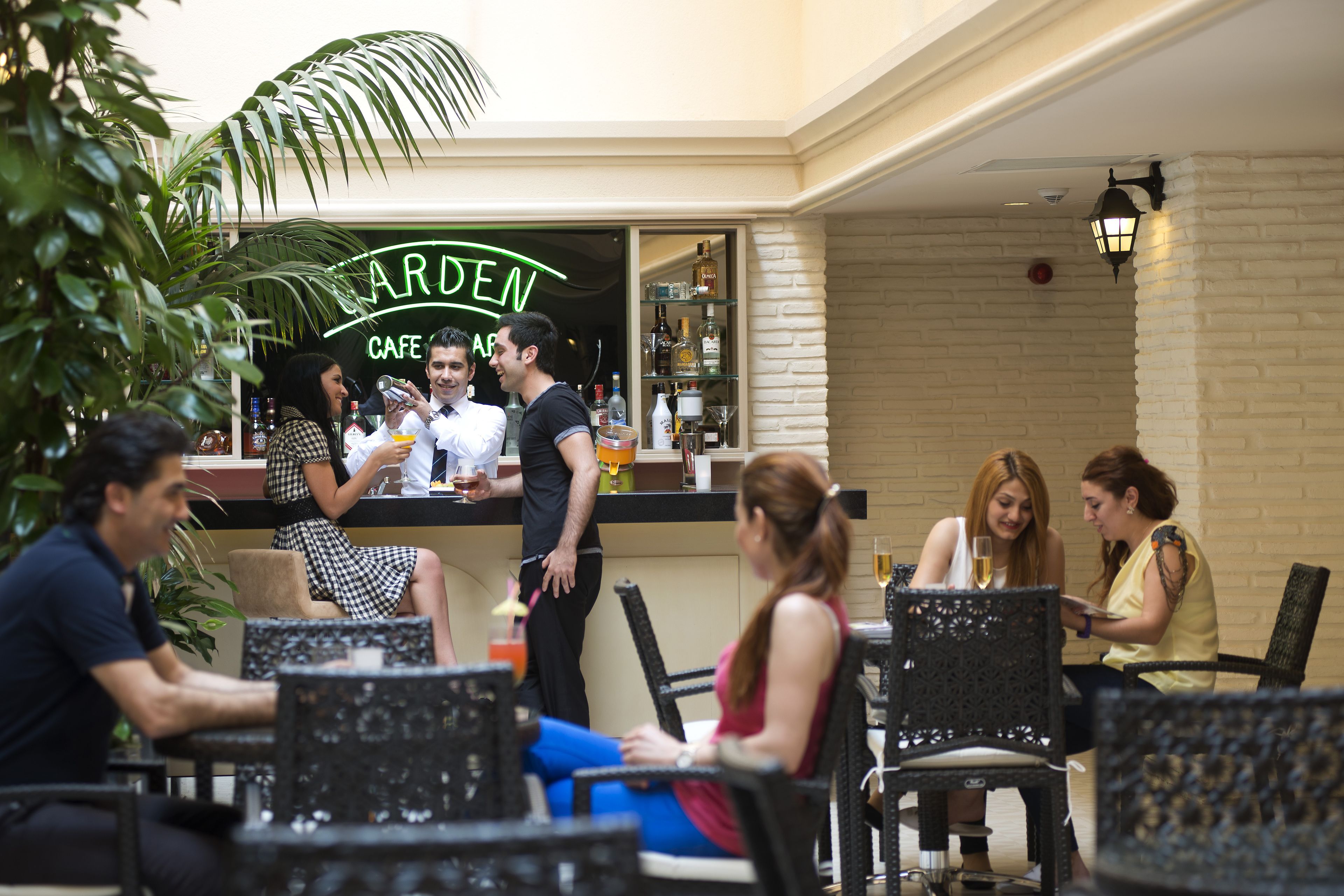 An outdoor cafe with a neon sign, wicker furniture, and a bar area.