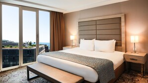 A hotel room with a large bed, two bedside lamps, a bench, and a view of the city through large windows. - Nidya Hotel Galataport (Istanbul)