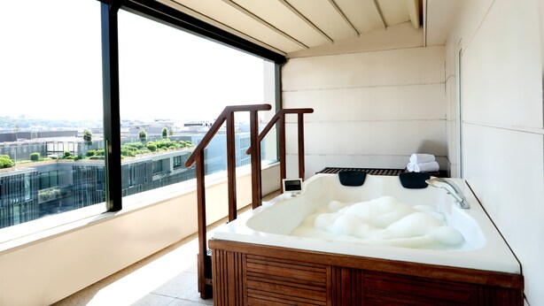 A modern bathroom with a large window, a wooden bathtub, and a view of the city. - Nidya Hotel Galataport (Istanbul)