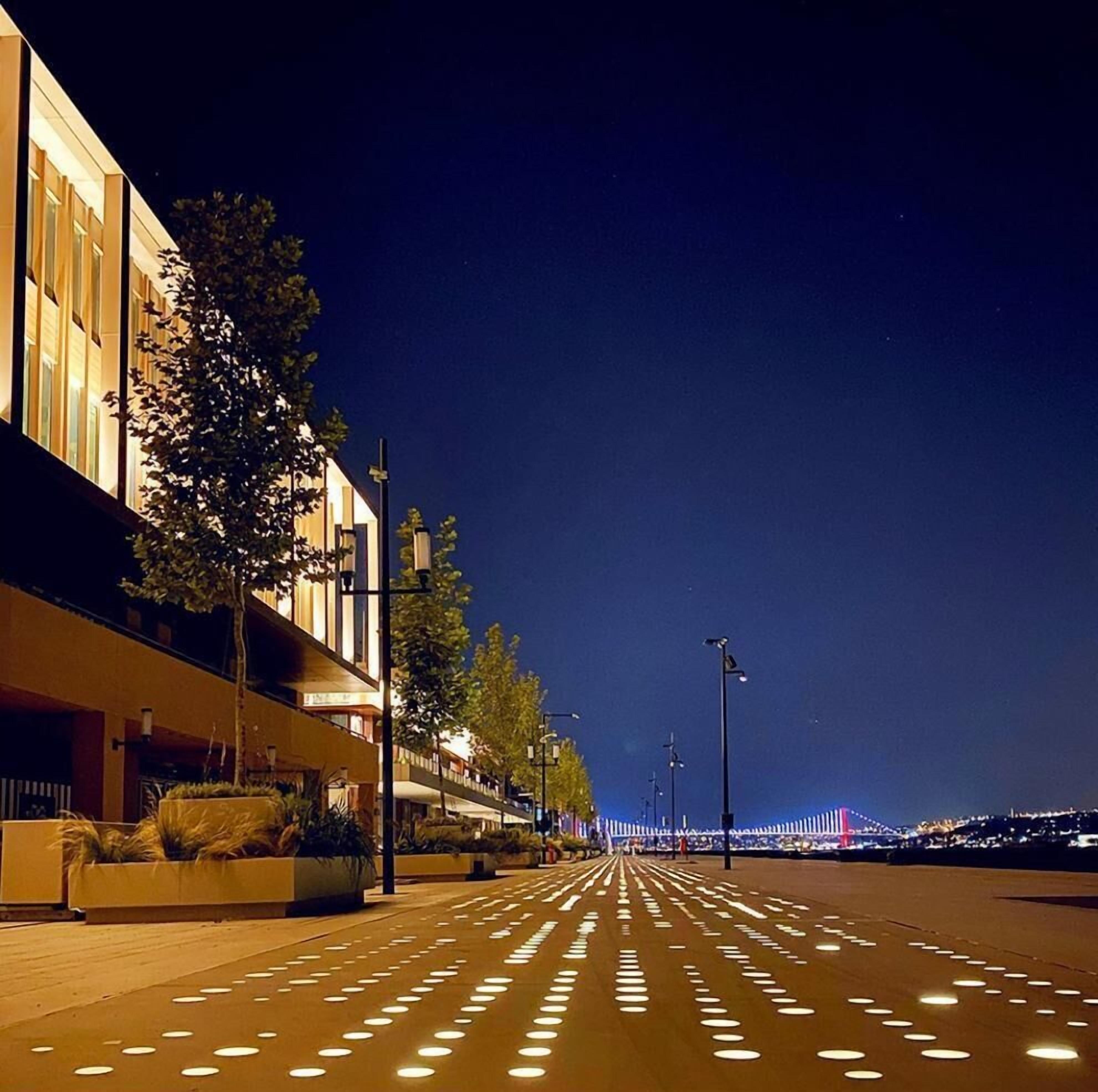 A nighttime street view with illuminated buildings and a bridge in the distance.