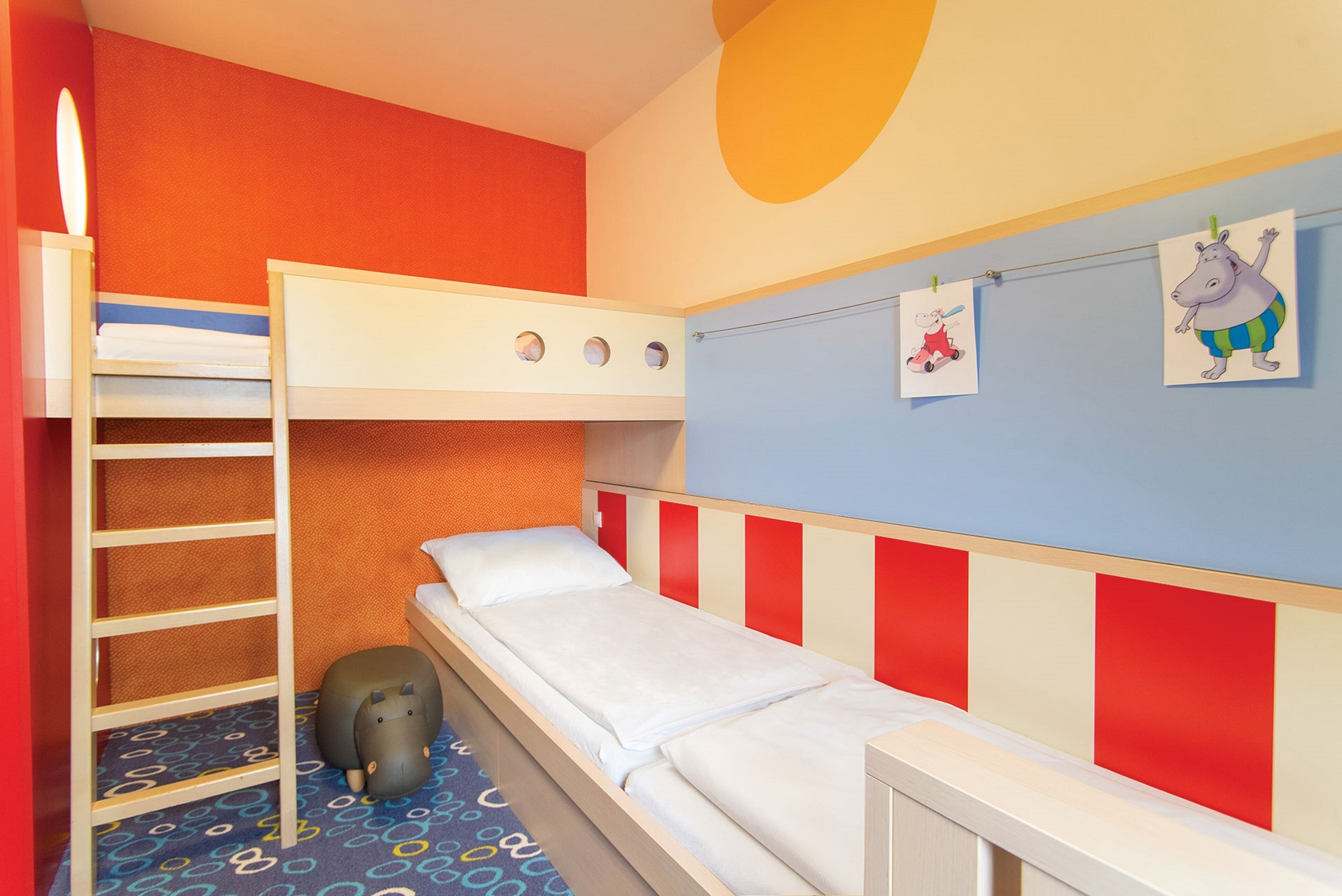 Ein Schlafraum mit Etagenbett, einer Sprossenleiter, einem kleinen Spielzeug und zwei Wandbildern.