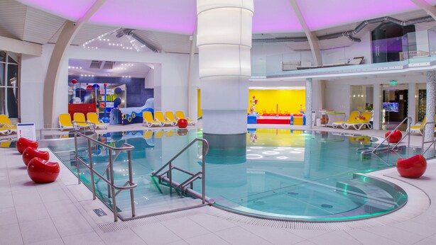 Una piscina interior con una fuente central, rodeada de sillas reclinables amarillas y asientos rojos.
