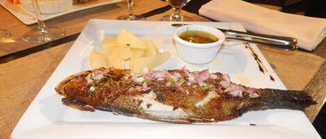 A plate with a grilled fish, boiled potatoes, and a small bowl of sauce.