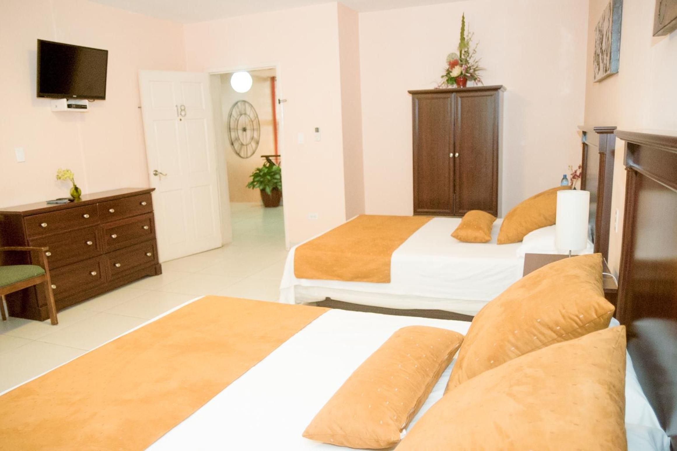 A bedroom with two beds, a dresser, a television, and a door leading to another room.