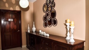 A conference room with a wooden door, a decorative mirror wall, a white vase, and two white candle holders. - Allamanda Hotel (Petionville)
