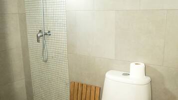 Et badeværelse med brusebad, toilet og en hylde med toiletartikler.