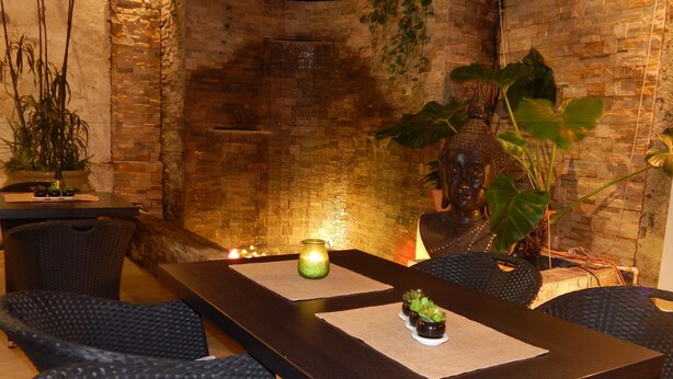 A dining area with a dark wooden table, wicker chairs, and a brick wall backdrop. - Allamanda Hotel (Petionville)