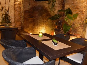 A dining area with a dark wooden table, wicker chairs, and a brick wall backdrop. - Allamanda Hotel (Petionville)